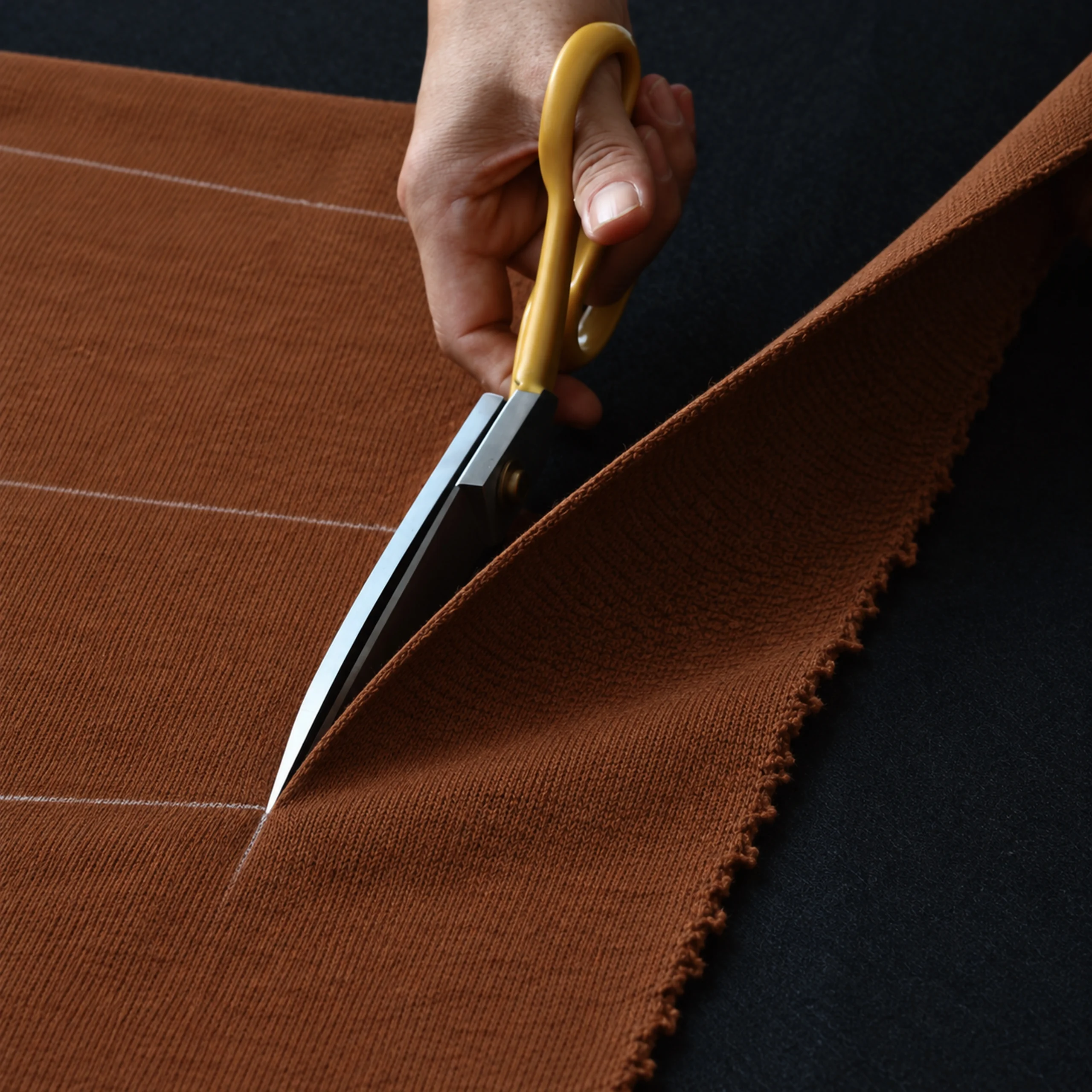 Scissors cutting brown fabric along marked garment pattern lines